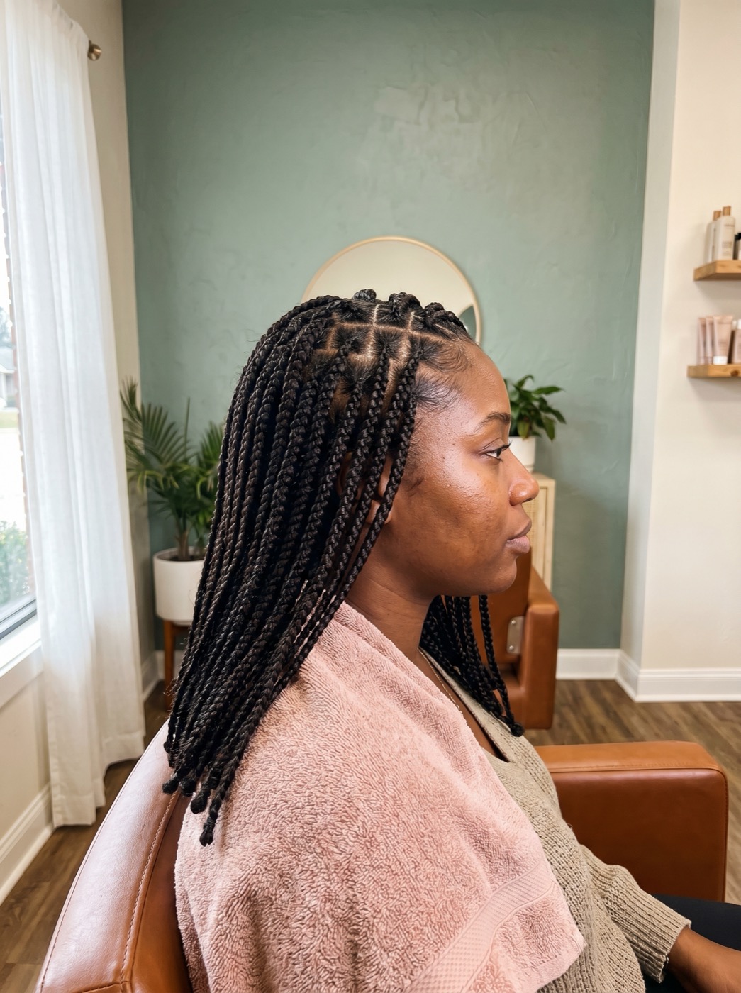 Black woman in side profile showing precise box braids parting and braid detail at a sage-toned styling station